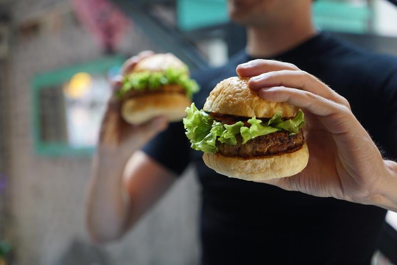 Two vegan burgers, each in the hand of a man in a black t-shirt
